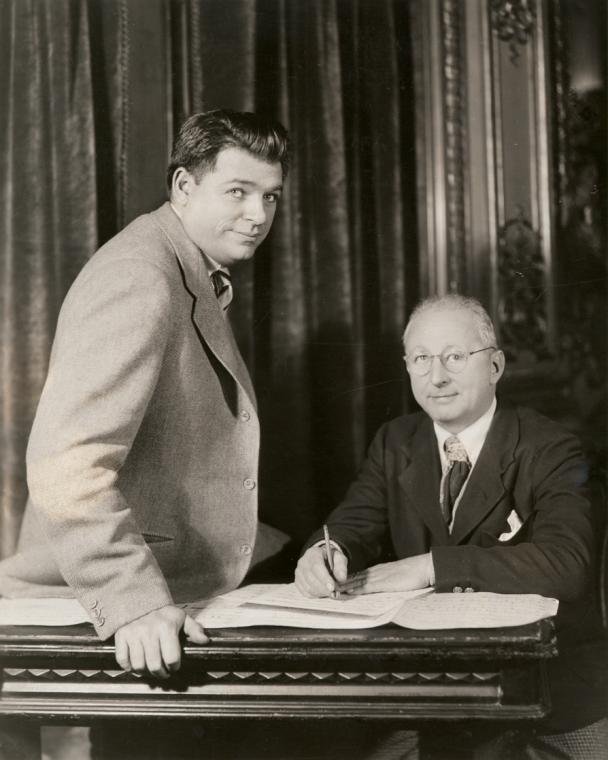 Oscar Hammerstein and Jerome Kern casually sit by a piano and look over sheet music.