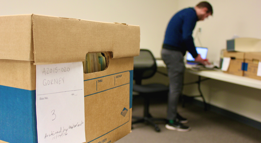 Bankers box of archival materials labeled Jay Gorney with a researcher in a blue sweater and grey pants exploring papers on a work table.