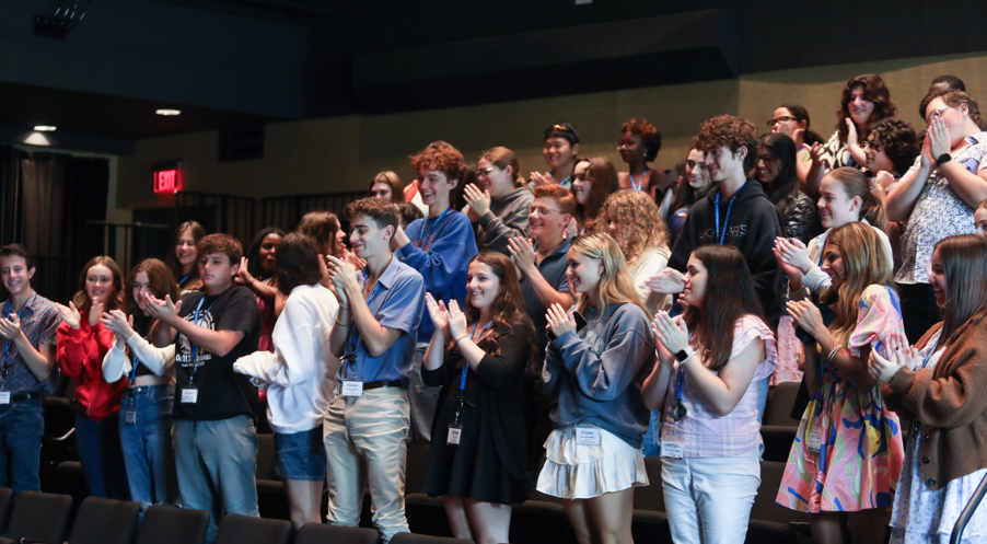 A group of high school students all stand and clap.