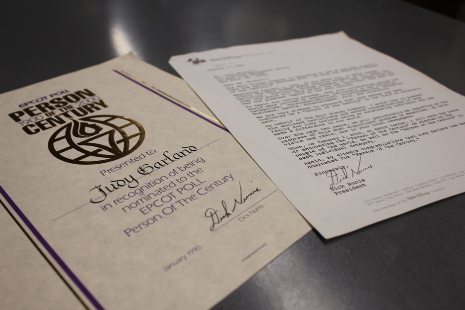 A certificate the the Epcot logo reads "Person of the Century: Judy Garland". A blurrled letter lays next to the certificate.